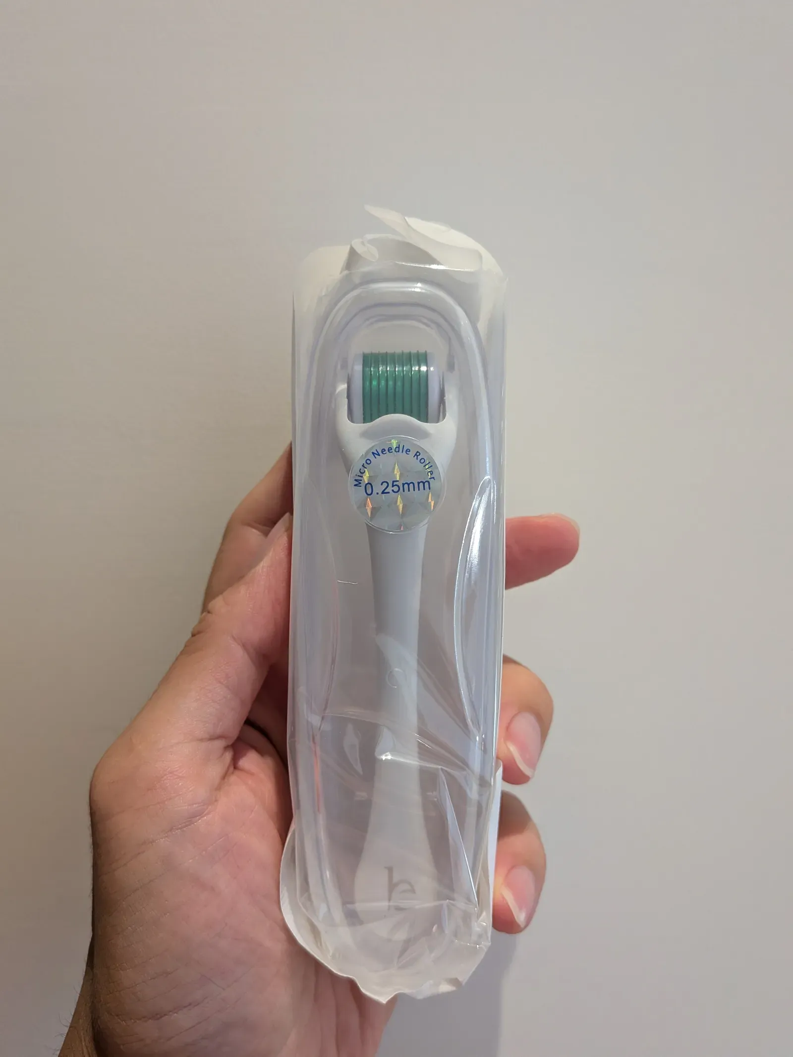 Hand holding a sealed dermaroller — the needle head sticker clearly displays the 0.25 mm length spec; for AGA you want a separate 1.5 mm tool