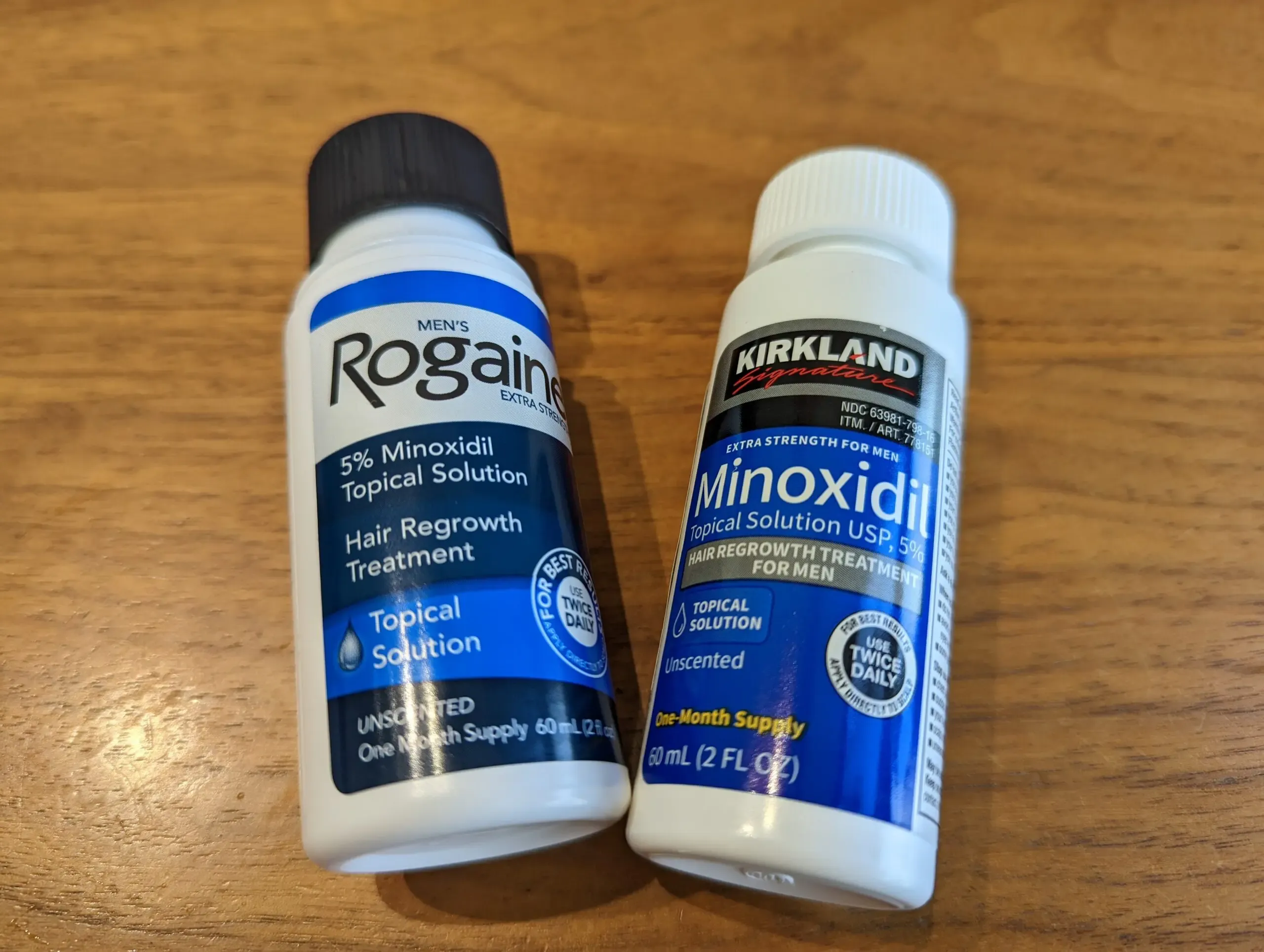 Side-by-side bottle comparison of Kirkland 5% Minoxidil and Rogaine 5% topical solution — both contain identical active ingredient