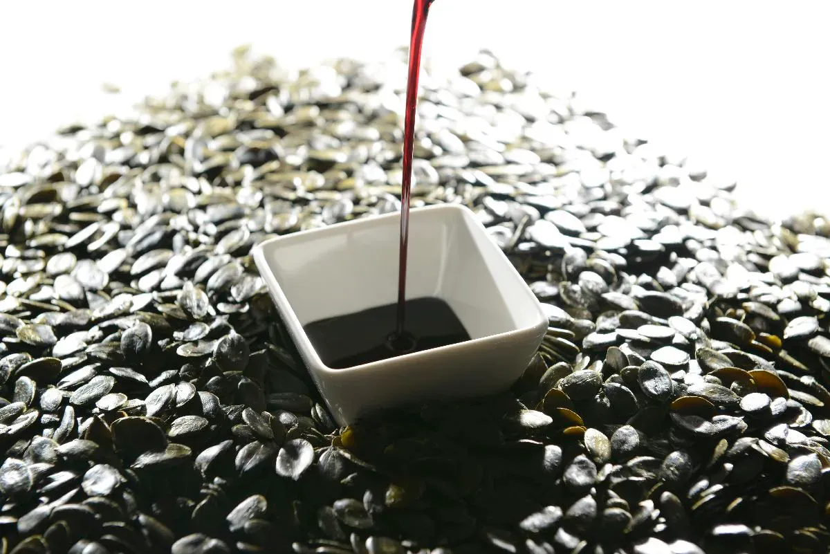 Cold-pressed pumpkin seed oil being poured — the deep amber color and characteristic reddish shimmer indicate high phytosterol content (Styrian Δ7-stigmasterol-rich variety)